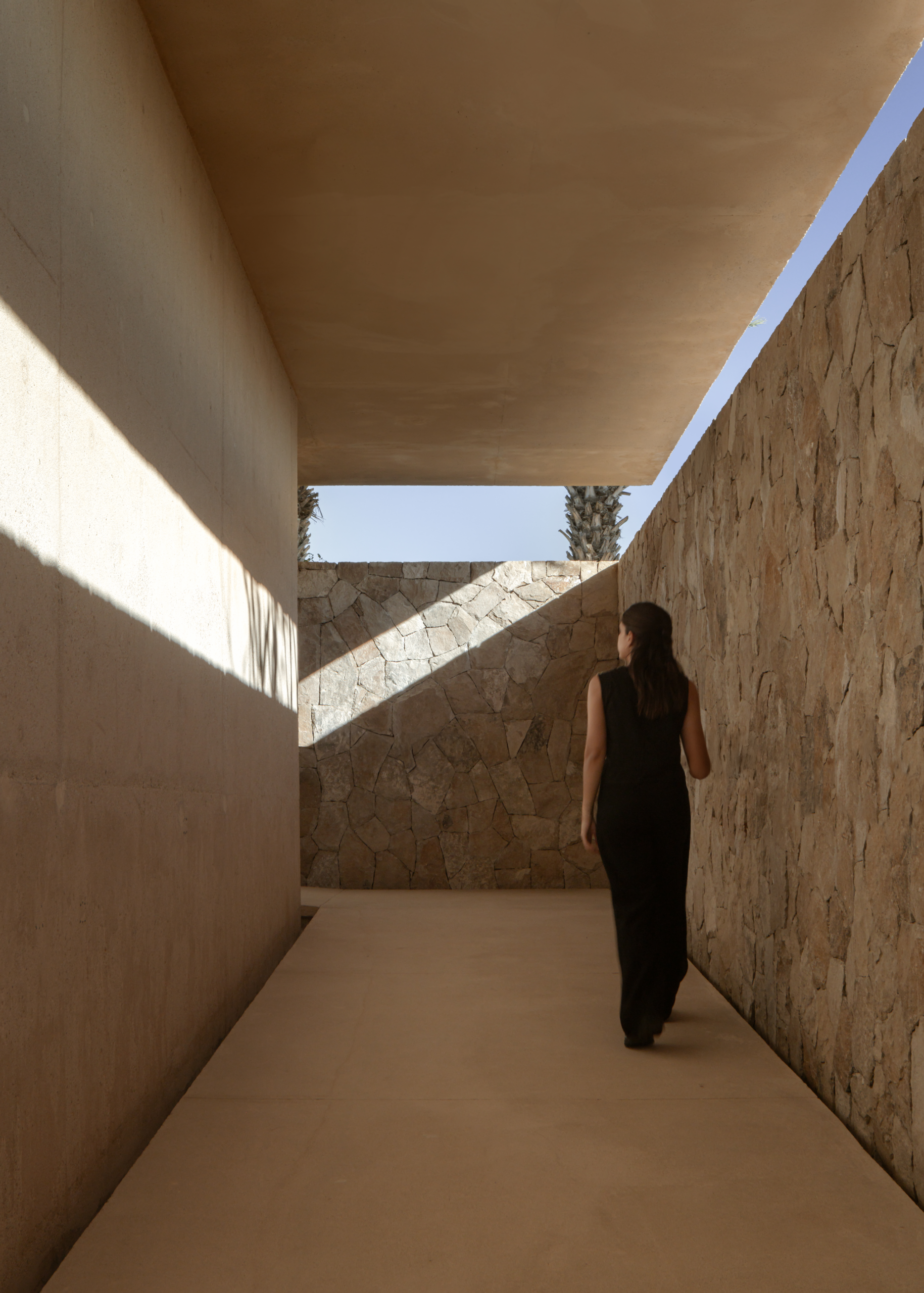 Person walking through a narrow stone and plaster corridor at Arte Abierto Baja gallery, Los Cabos. By Sordo Madaleno.