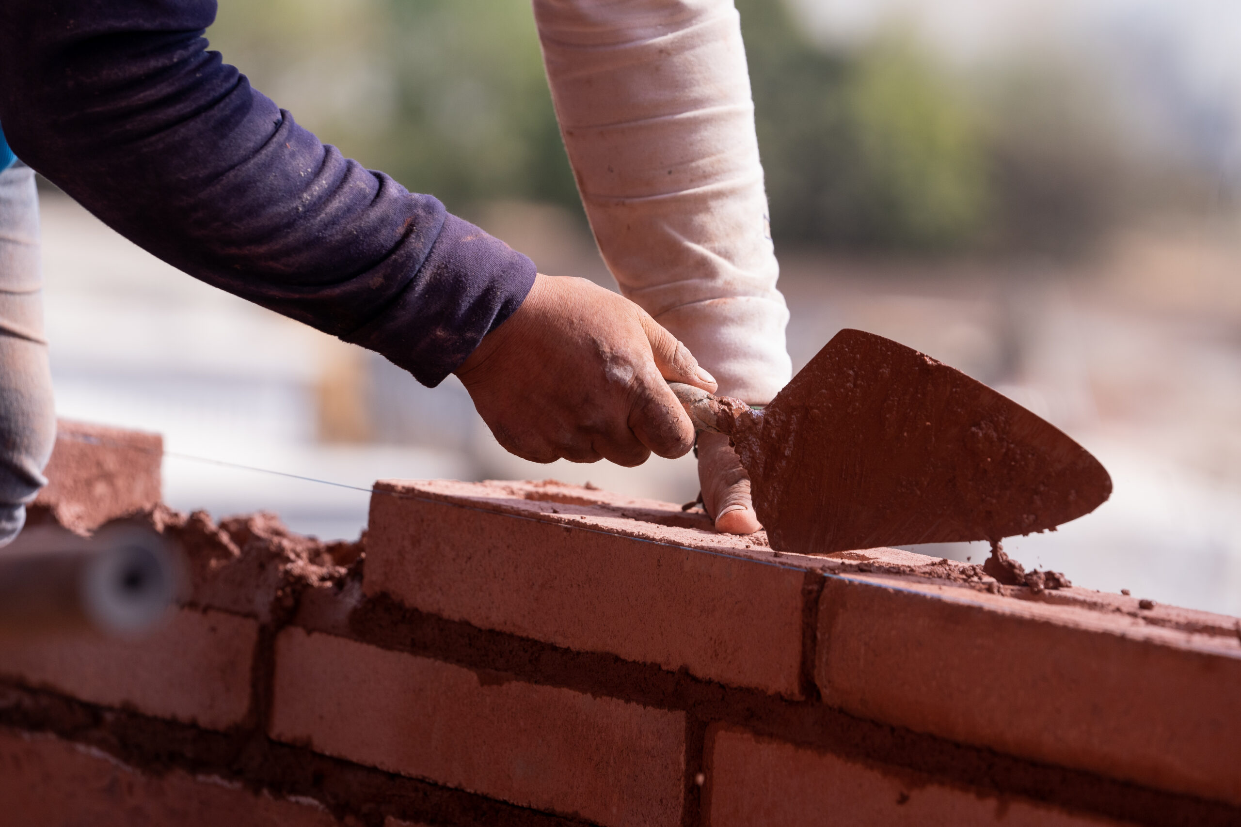 Hand holding trowel while laying red bricks