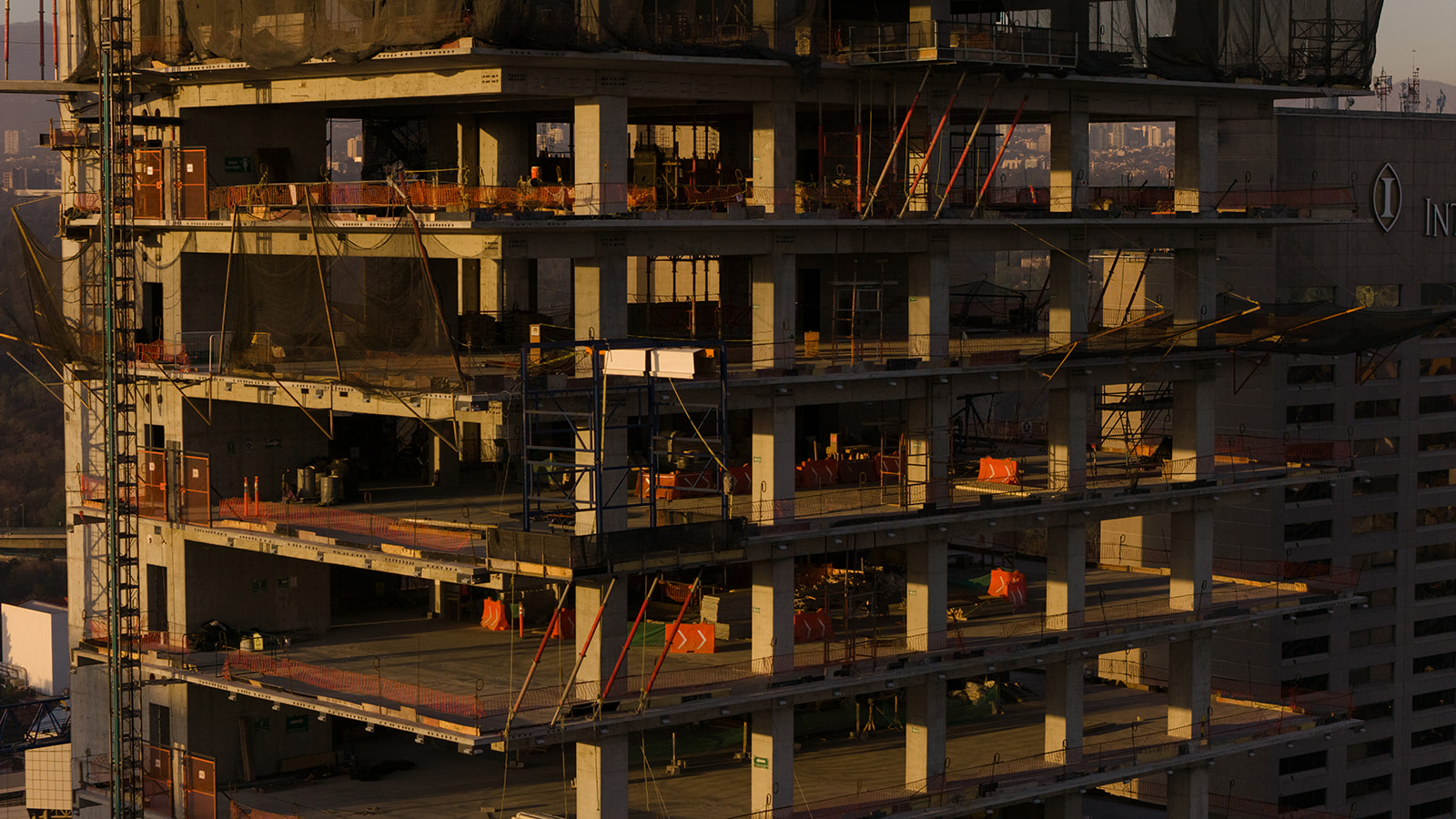 Exterior view of the Park Hyatt Mexico City under construction, showing concrete floor plates and tower crane at dusk, with the city skyline in the background.
