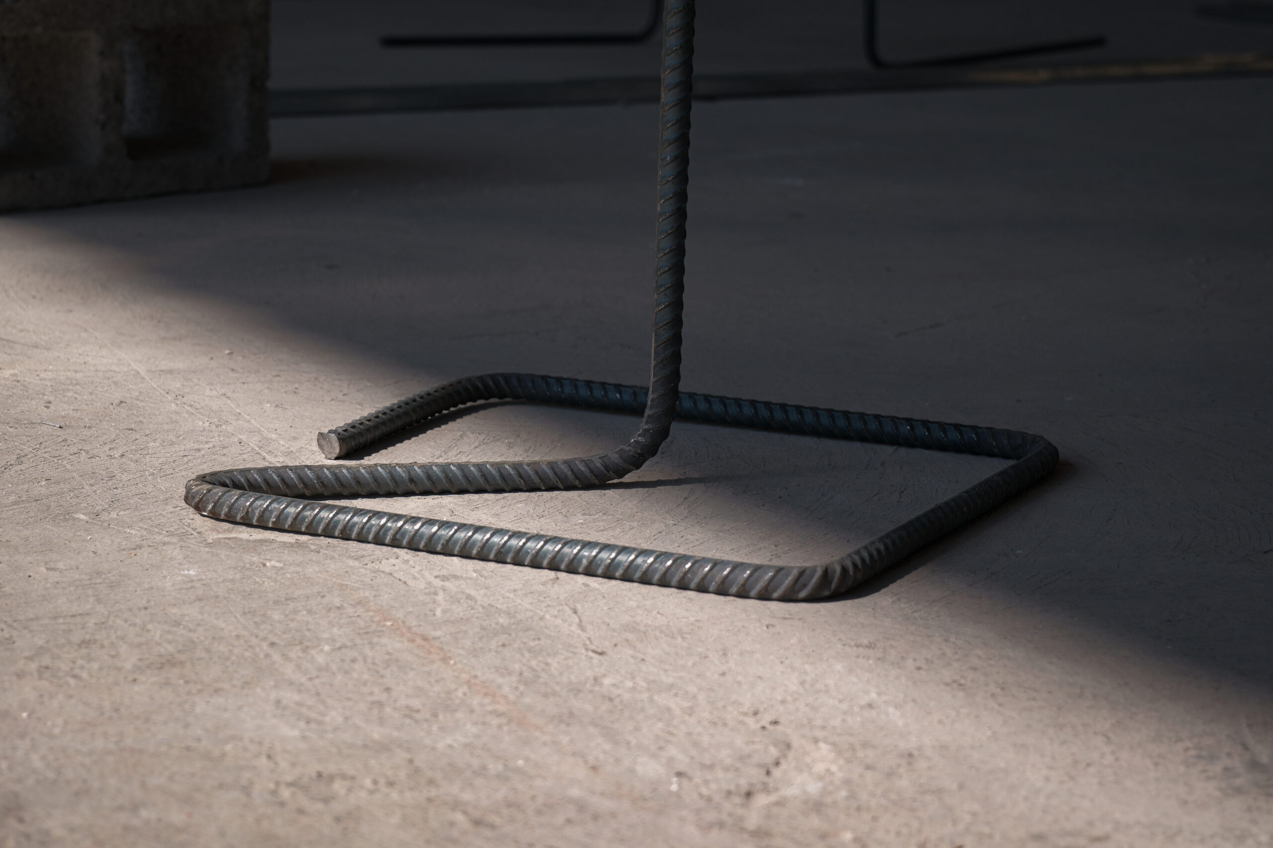 Detalle de una base de barra de hormigón doblada que descansa sobre un Concreto , parte del mobiliario expositivo diseñado en colaboración con fierreros para la exposición «Memory as Material».