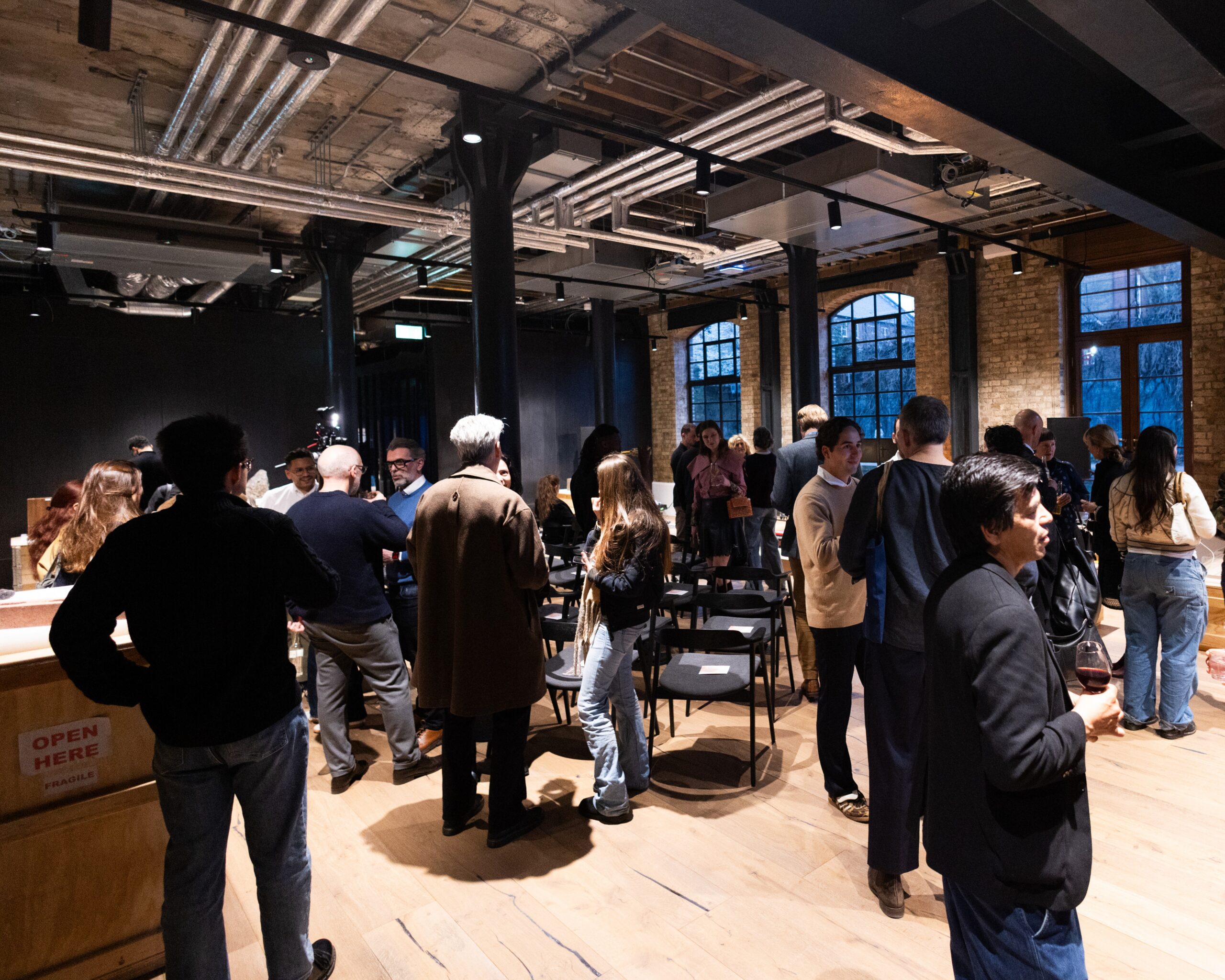 a group of people standing and mingling in a high ceiling brick and steel building