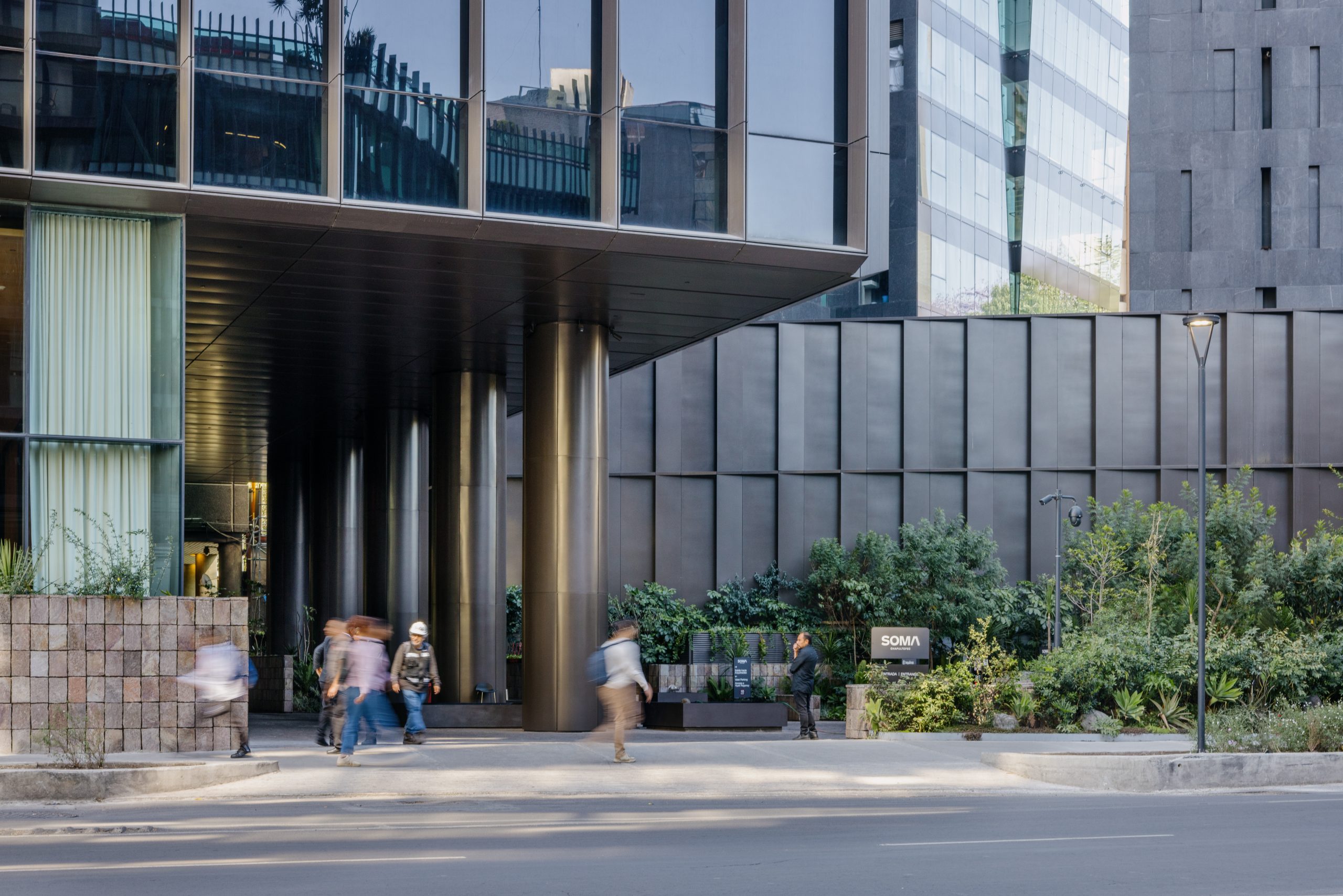 Entrada a pie de calle del Park Hyatt México D. F., con columnas de bronce, fachada acristalada y zona ajardinada en el perímetro del Paseo de la Reforma. Obra de Sordo Madaleno.