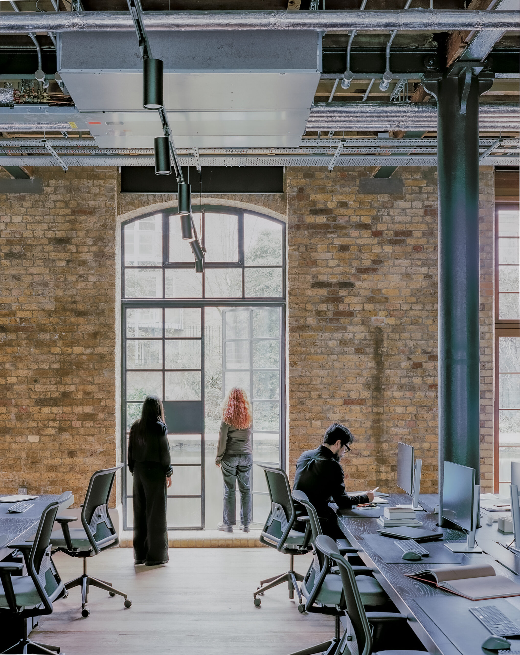 Sordo Madaleno London Studio Interior with large windows and brick wall. Long design desks with work stations