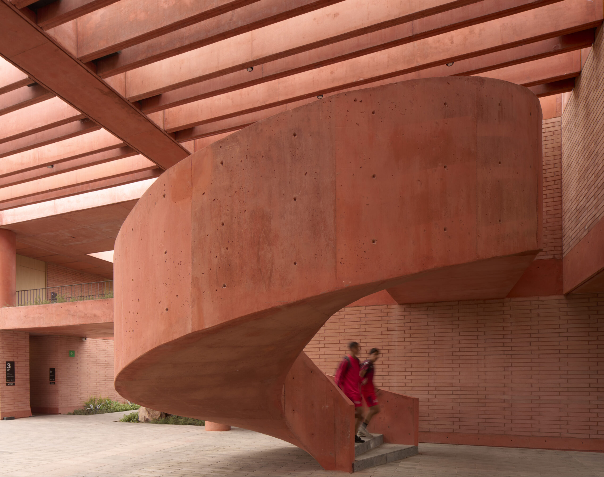 Sculptural concrete staircase in red pigmented concrete at Academia Atlas FC training campus, Guadalajara. By Sordo Madaleno.