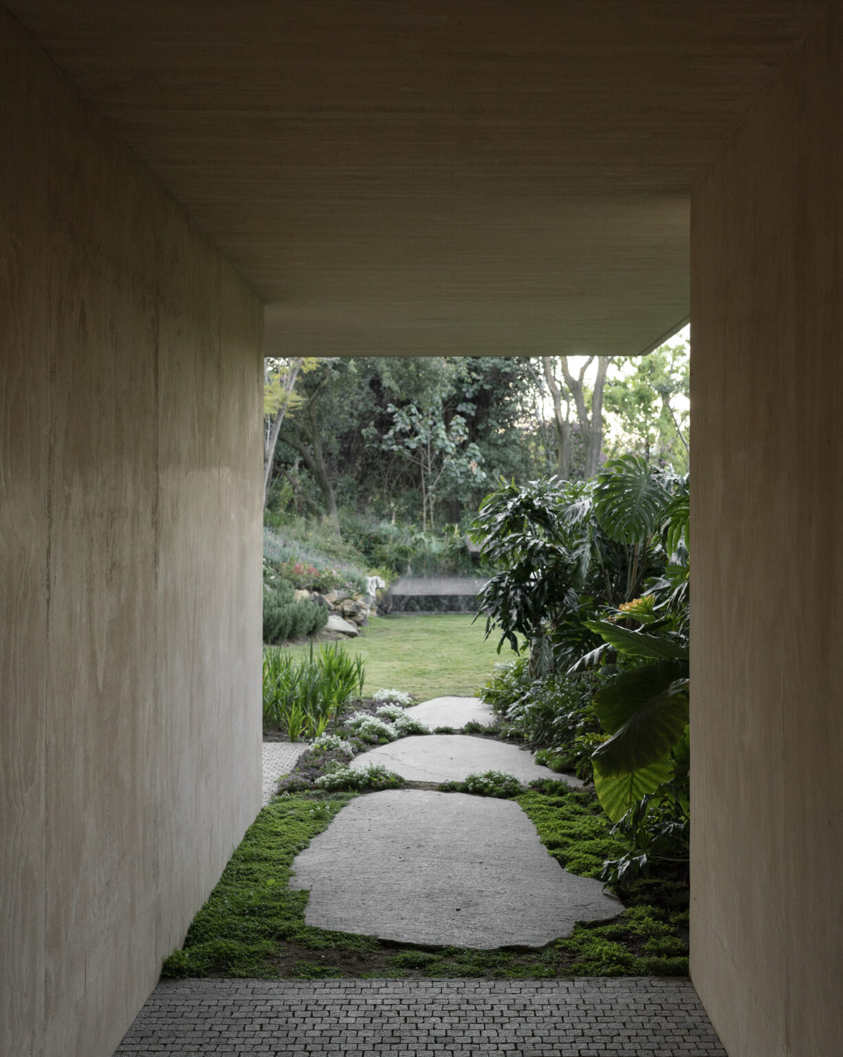 Sordo Madaleno — Stone pathway through a lush garden framed by a concrete opening at Casa SM, Mexico City. By Sordo Madaleno.