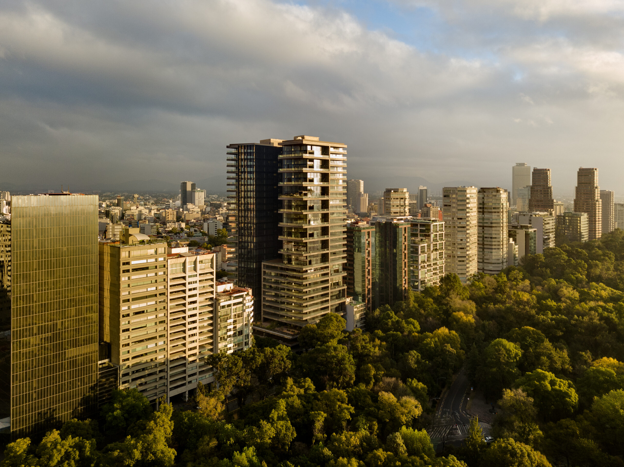 Aerial drone photo of Rubén Darío 255 by Sordo Madaleno, its twin residential towers rising above Mexico City's skyline beside the tree canopy of Bosque de Chapultepec at golden hour.