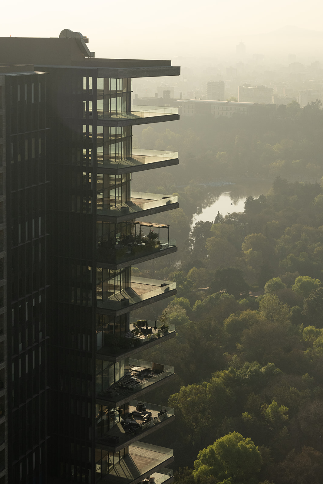 Close-up aerial photo of Rubén Darío 255's tiered terraces by Sordo Madaleno, glowing in hazy golden light above the lake and tree canopy of Bosque de Chapultepec.