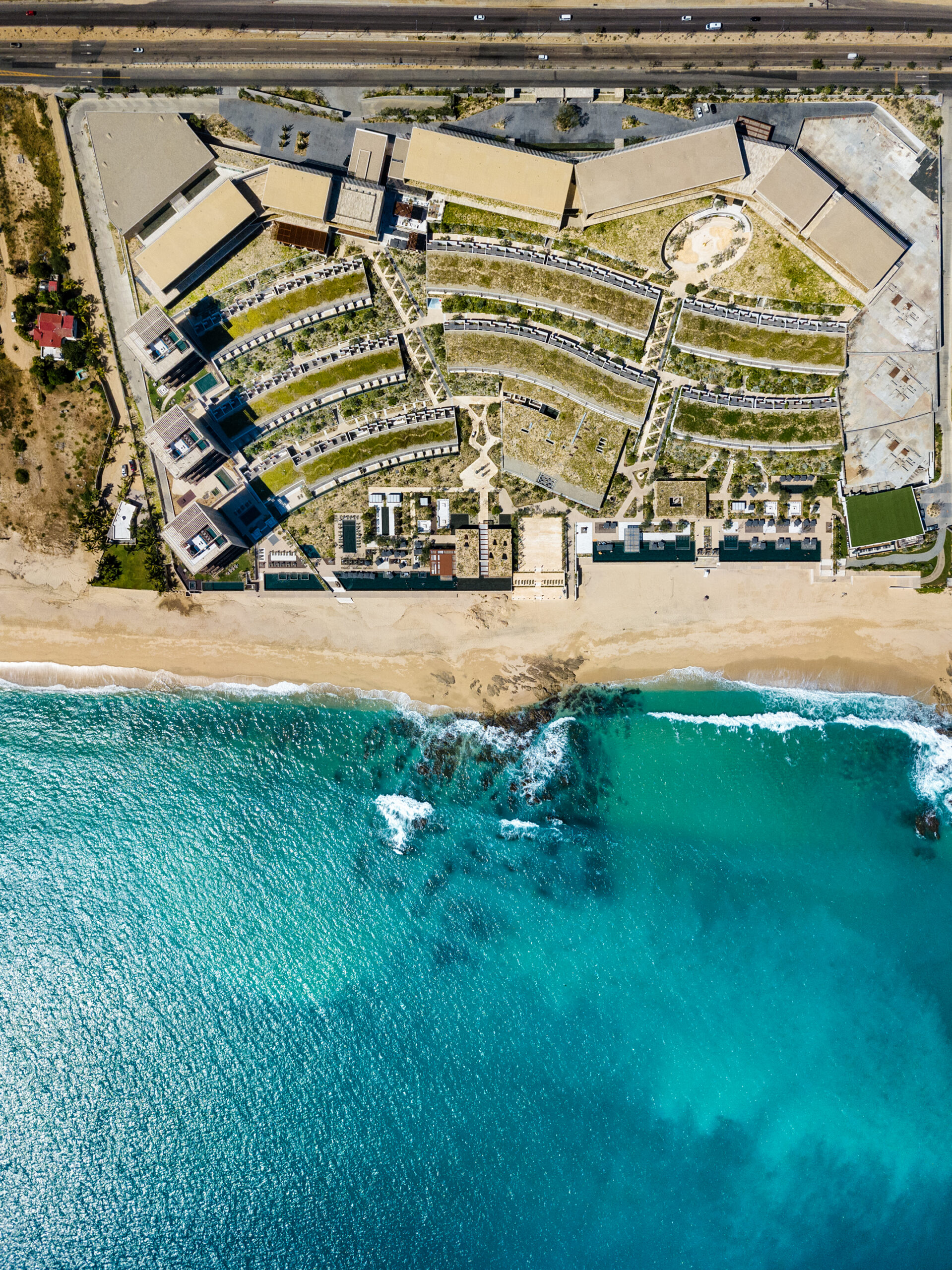 Aerial view of Solaz Los Cabos resort's fan-shaped room wings between the highway and the Pacific coastline