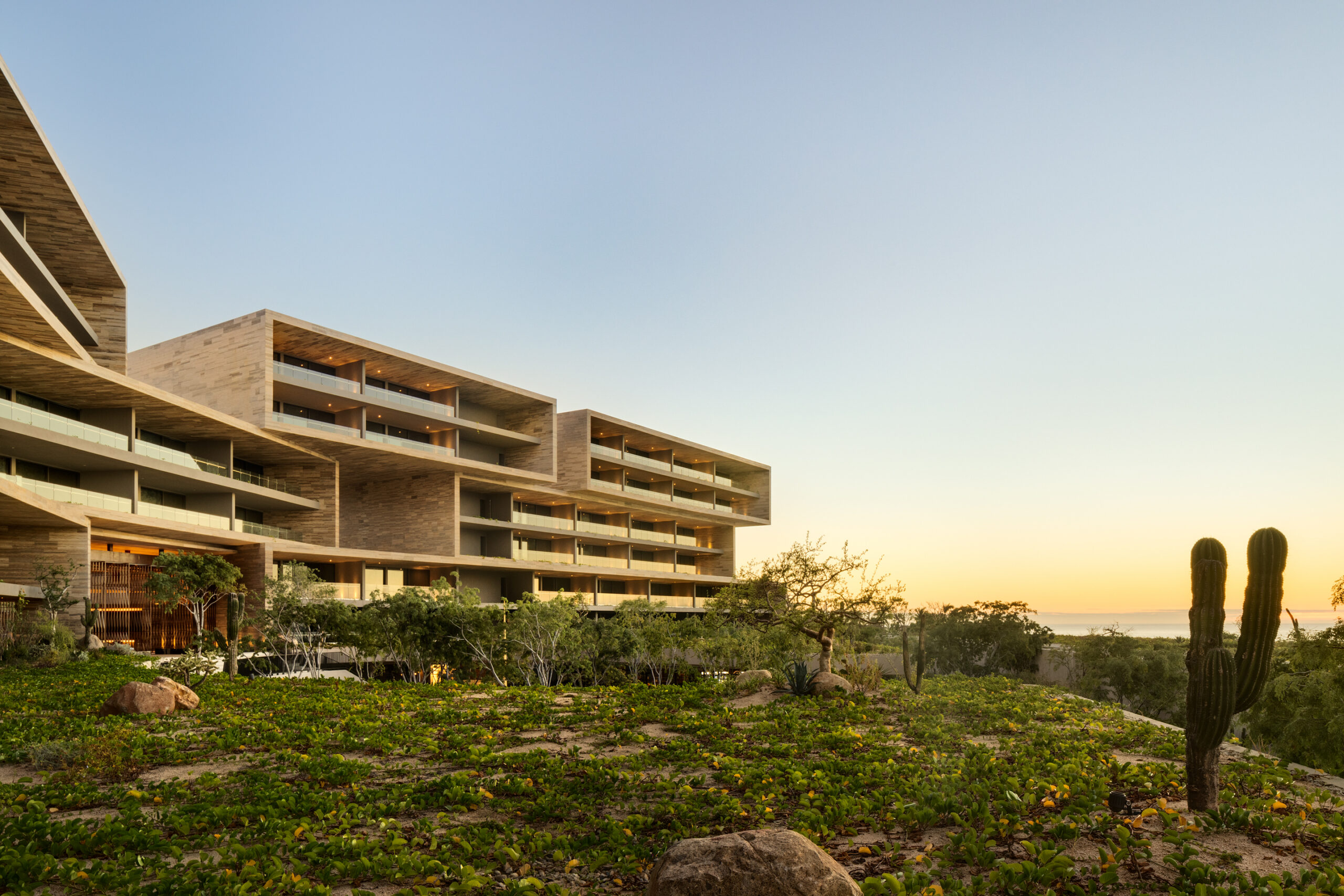 Stone-clad guest room wing at Solaz Los Cabos at dusk, cantilevered terraces overlooking the desert