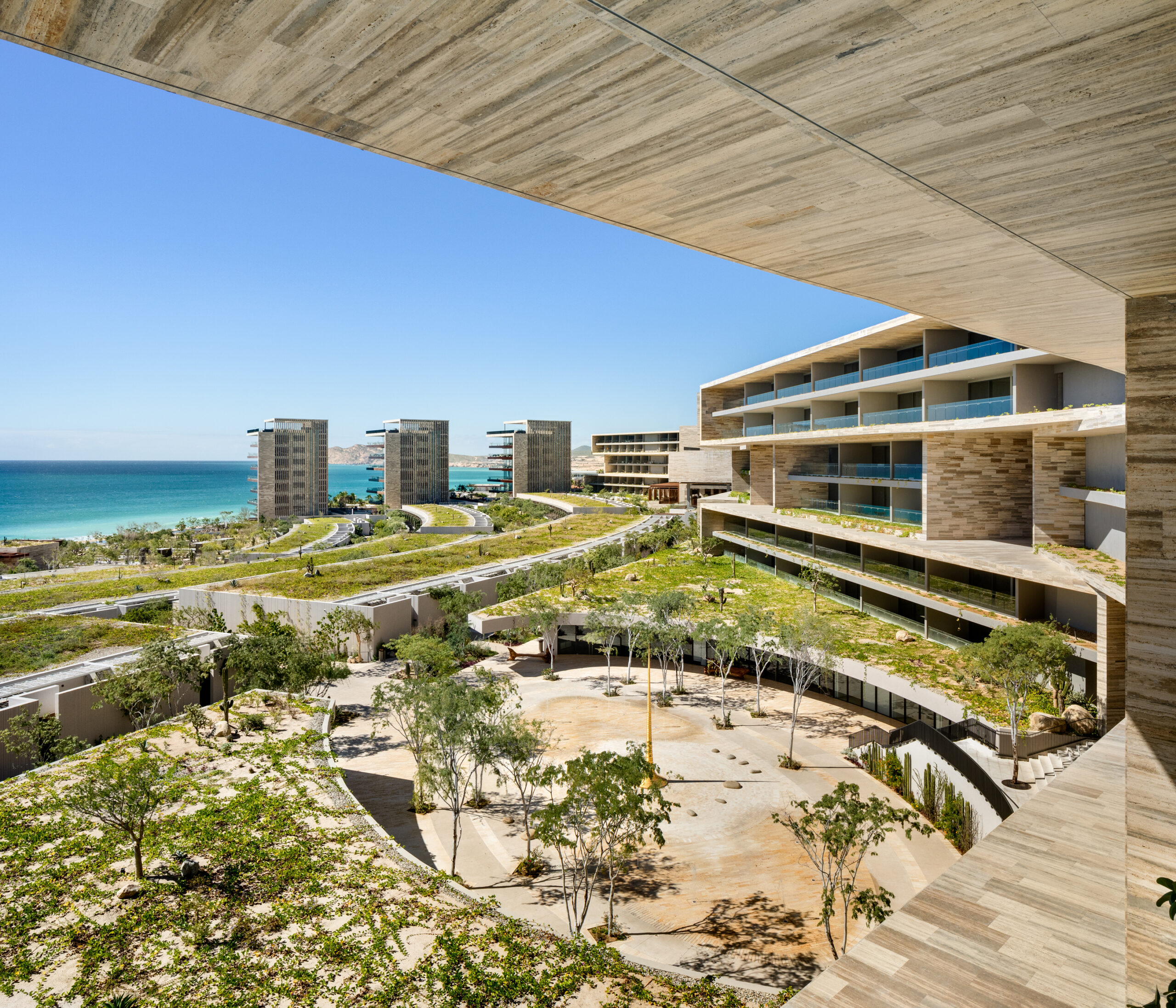 View from beneath a cantilevered stone terrace at Solaz Los Cabos, overlooking the central courtyard, residential towers, and the ocean