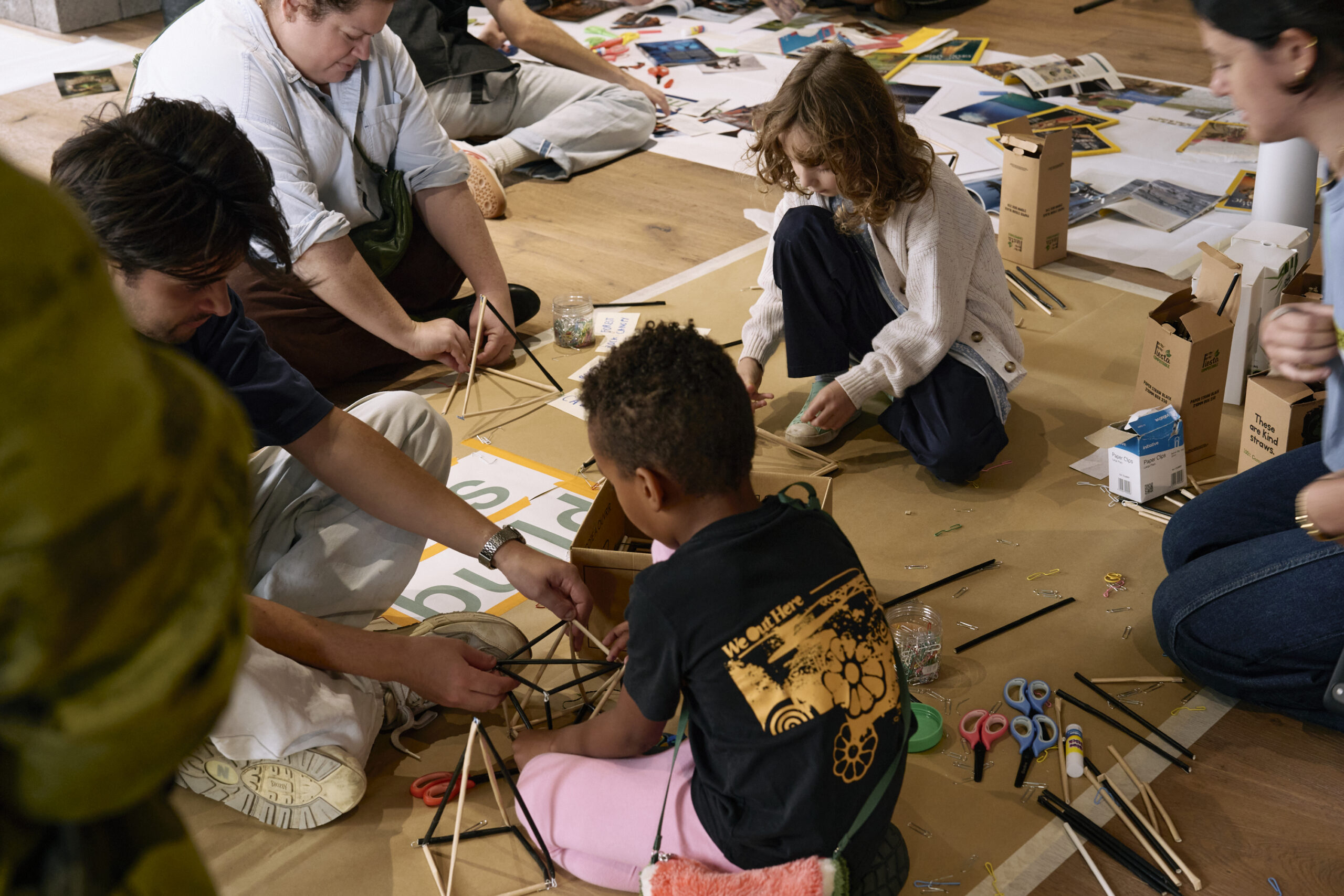 Adultos y niños construyendo juntos estructuras de paja en el suelo durante el taller «Straw-ctural Designers», en el Open House Festival 2026, Londres