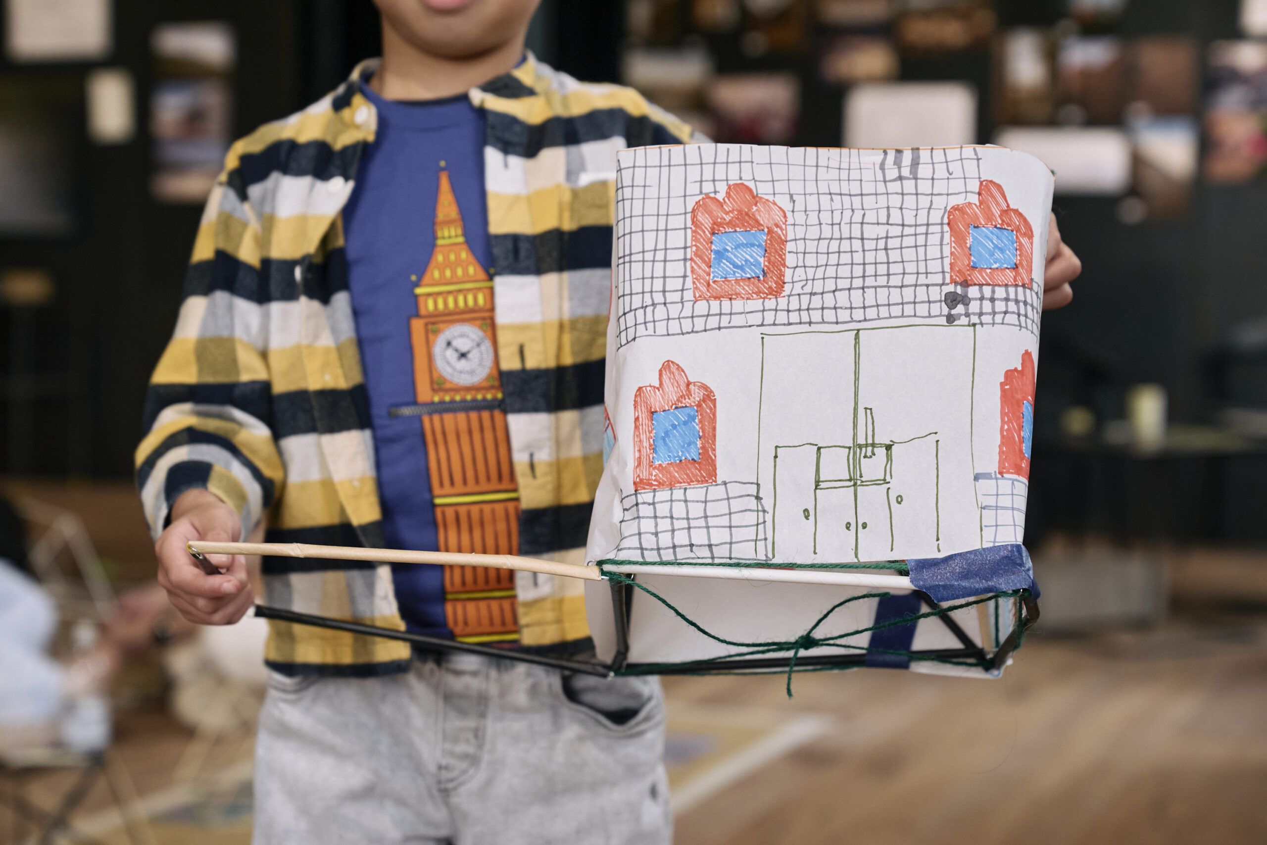 Niño sosteniendo una maqueta de cartón con la fachada de un edificio dibujada a mano en el taller «Straw-ctural Designers», Festival Open House 2026, Londres